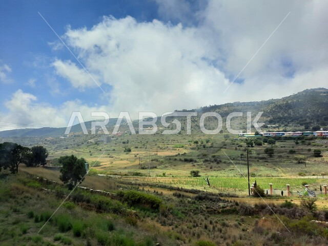 المدرجات الزراعية والحقول والنباتات الخضراء في جبال عسير، منظر السحب والغيوم البيضاء في السماء، القمم والمرتفعات الجبلية في مدينة ابها، مدن وأماكن سياحية طبيعية في المملكة العربية السعودية، القرى السكنية والبيوت والمنازل المبنية أعلى الجبل