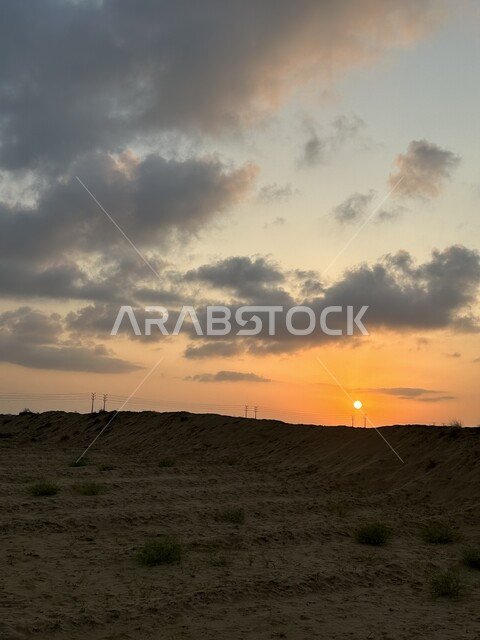 Spending enjoyable times in the desert areas in the Kingdom of Saudi Arabia, a tourist wilderness trip in the desert, the sunset scene in a sky full of clouds, thorny plants in deserts and dry areas.
