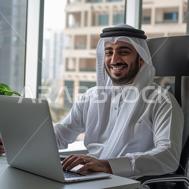 مهن ووظائف ادارية مكتبية، دمج العمل مع التقنية والتكنولوجيا، إدارة شؤون الأعمال وتنظيمها عبر الاجهزة التقنية، رجل اعمال عربي خليجي سعودي يرتدي الزي التقليدي والغترة يعمل على الحاسوب المحمول داخل المكتب