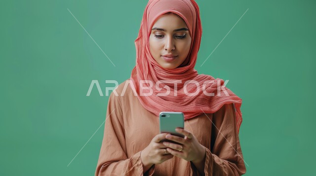 الاهتمام بالمظهر الخارجي, بورتريه مقرب لإمرأة خليجية سعودية ترتدي الحجاب تقوم بتصفح مواقع التواصل الاجتماعي عبر الهاتف المحمول، الدردشة مع العائلة والأصدقاء، الإجابة والرد على الرسائل عبر الجوال، خلفية خضراء