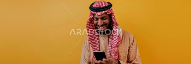 تصفح الانترنت ومواقع التواصل الاجتماعي، التحدث والدردشة مع الأهل والأصدقاء عبر الموبايل، ايماءات السعادة والسرور، بورتريه مقرب لرجل عربي خليجي سعودي مبتسم يرتدي الثوب التقليدي يحمل بيده الهاتف المحمول، خلفية صفراء