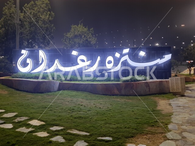 An illuminated welcome sign on the gate of Raghadan Forest Park in the city of Al-Baha, interest in illuminating public gardens, afforestation and planting green plants in the cities of the Kingdom of Saudi Arabia, natural family recreational places, spending enjoyable time in nature and the outdoors.