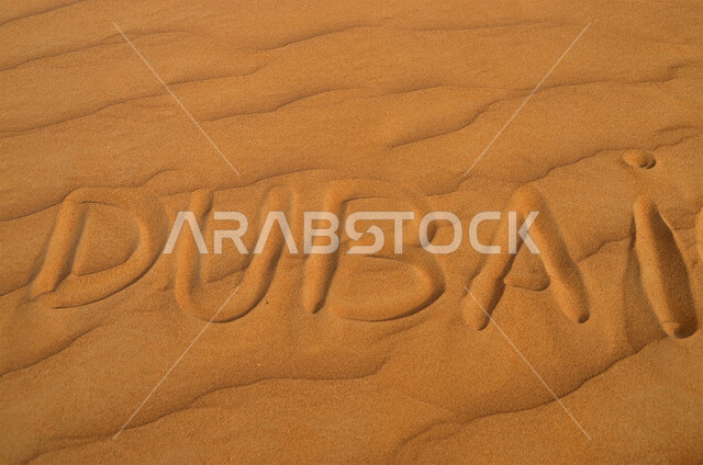 Sand dunes in the desert, a close-up of the word Dubai in the English language on the soft golden sand, the desert regions and the natural desert environment in the United Arab Emirates, nature backgrounds