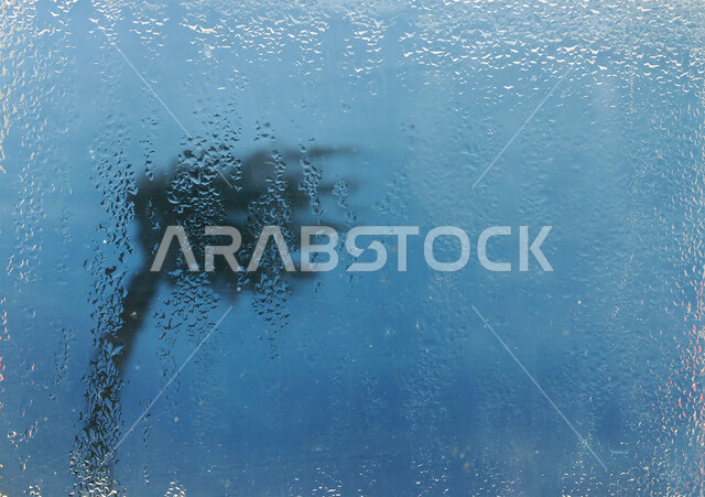 منظر قطرات المطر على النافذه، نخله مائله في وسط الأجواء الشتويه والرياح العاتيه في دبي وأبوظبي في الامارات العربيه المتحده، خلفيه زرقاء ضبابيه