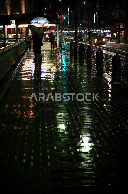 التجول والمشي وقت المطر، أماكن ومعالم تاريخية سياحية في الإمارات العربية المتحدة، الاجواء الشتوية الباردة في دبي، صورة ليلية من الجانب لشخص يحمل مظلة للوقاية من الامطار