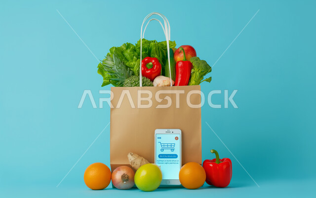 Modern e-commerce, marketing products through social networking sites, shopping and purchasing household needs through a mobile phone, a paper bag full of vegetables and healthy foods with a mobile phone next to it, fast delivery of orders, blue background
