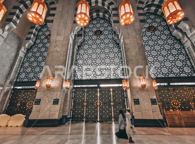 مجموعة من المسلمين يتجولون في ممرات توسعة الملك عبدالله للحرم المكي الشريف ,اماكن دينيه مقدسة, الزخارف الجبسيه الاسلاميه الفاخره على الأسقف ,إدخال النجف على طراز الفوانيس العربيه والثريا في التصاميم المعماريه، صورة من داخل المسجد الحرام بمكة المكرمة في السعودية