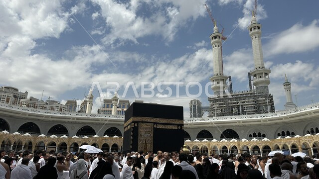 مآذن المسجد الحرام في مكة المكرمة بالمملكة العربية السعودية، أداء مناسك الحج والعمرة، العبادة والتقرب إلى الله، معالم دينية إسلامية مقدسة، طواف الحجاج حول الكعبة في ساحة الحرم المكي الشريف في النهار