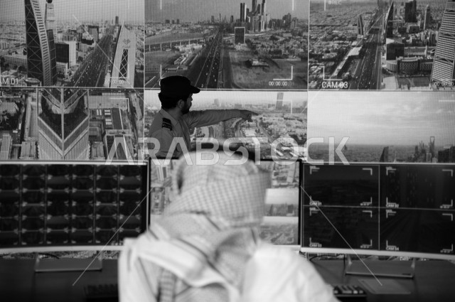 A Saudi Gulf man runs the security section, tracks surveillance cameras with the security man who works at the place, wears traditional Saudi uniforms, maintains security and reassurance, guards and safety