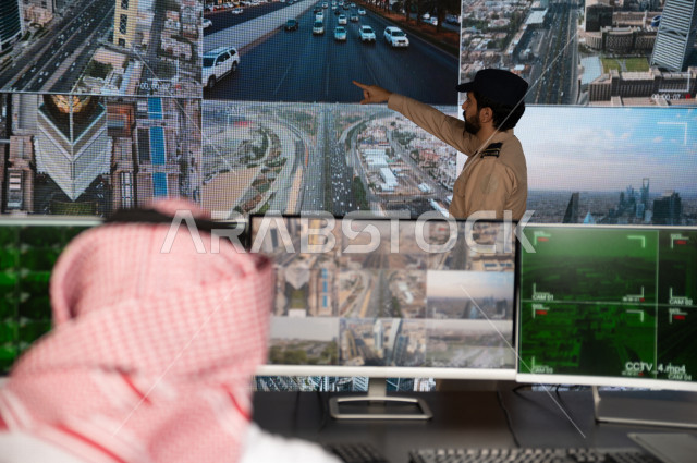 رجل سعودي خليجي يدير القسم الامني  ، يقوم بتتبع كاميرات المراقبة مع رجل الامن الذي يعمل بالمكان ،  ، يرتدي الزي السعودي التقليدي ، الحفاظ على الامن و الطمأنينة ، حراسة و امان 