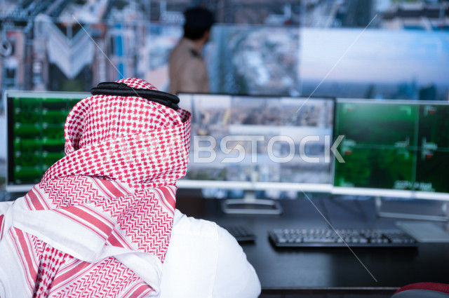 رجل سعودي خليجي يدير القسم الامني  ، يقوم بتتبع كاميرات المراقبة مع رجل الامن الذي يعمل بالمكان ،  ، يرتدي الزي السعودي التقليدي ، الحفاظ على الامن و الطمأنينة ، حراسة و امان 