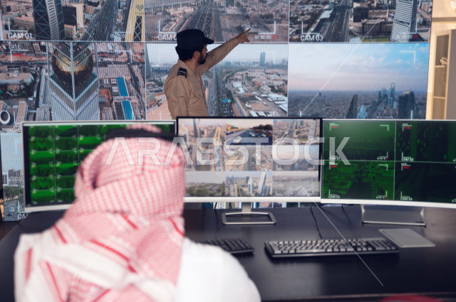 رجل سعودي خليجي يدير القسم الامني  ، يقوم بتتبع كاميرات المراقبة مع رجل الامن الذي يعمل بالمكان ،  ، يرتدي الزي السعودي التقليدي ، الحفاظ على الامن و الطمأنينة ، حراسة و امان 