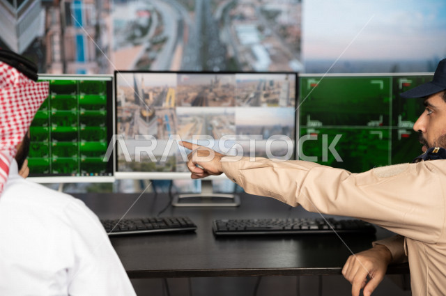 رجل سعودي خليجي يدير القسم الامني  ، يقوم بتتبع كاميرات المراقبة مع رجل الامن الذي يعمل بالمكان ،  ، يرتدي الزي السعودي التقليدي ، الحفاظ على الامن و الطمأنينة ، حراسة و امان 
