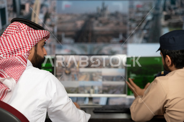 رجل سعودي خليجي يدير القسم الامني  ، يقوم بتتبع كاميرات المراقبة مع رجل الامن الذي يعمل بالمكان ،  ، يرتدي الزي السعودي التقليدي ، الحفاظ على الامن و الطمأنينة ، حراسة و امان 
