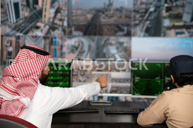 A Saudi Gulf man runs the security section, tracks surveillance cameras with the security man who works at the place, wears traditional Saudi uniforms, maintains security and reassurance, guards and safety
