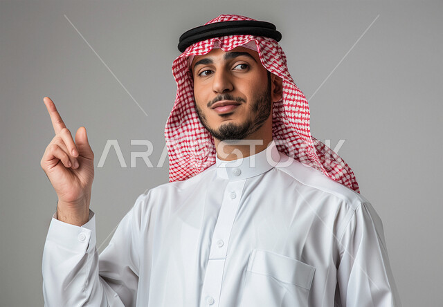 حركات وايماءات وجه ويدين مختلفة، الاشارة الى شيء ما، بورتريه مقرب لرجل عربي خليجي سعودي يرتدي الشماغ والثوب التقليدي يرفع اصبعه للأعلى، خلفية رمادية