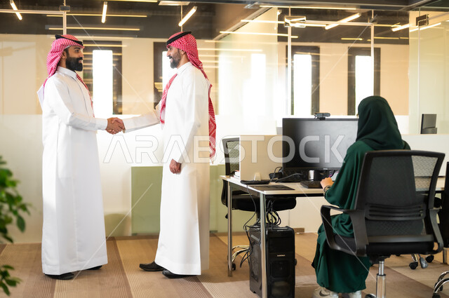 الترحيب والسلام وإلقاء التحية، رجلين عربيين خليجيين سعوديين مبتسمين يرتديان الشماغ والثوب التقليدي يتصافحان بإيماءات السرور بنجاح الصفقة، الوحدة والتفاعل الجماعي لتحقيق أهداف الشركة وحل المشكلات، مهن و وظائف مكتبية