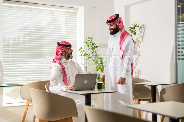 إنجاز المهام عبر الحاسوب المحمول، مناقشة المشاريع ومتابعة إستراتيجية العمل، موظفان عربيان خليجيان سعوديان يرتديان الزي التقليدي يقومان بمراجعة البحوث العلمية، مهن ووظائف مكتبية سعودية، مفهوم إدارة الأعمال، تحقيق أهداف الشركة