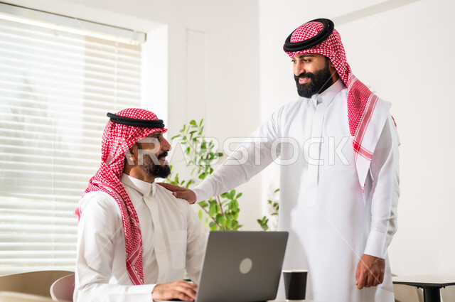 إستخدام الحاسوب المحمول لإنجاز المهام، مناقشة المشاريع ومتابعة إستراتيجية العمل، موظفان عربيان خليجيان سعوديان يرتديان الزي التقليدي يقومان بمراجعة البحوث العلمية، مهن ووظائف مكتبية سعودية، مفهوم إدارة الأعمال، تحقيق أهداف الشركة
