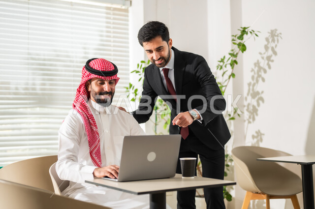تحقيق أهداف الشركة، مفهوم إدارة الأعمال، إنجاز المهام عبر الحاسوب المحمول، مناقشة المشاريع ومتابعة إستراتيجية العمل، موظفان عربيان خليجيان سعوديان يرتديان الزي التقليدي يقومان بمراجعة البحوث العلمية، مهن ووظائف مكتبية سعودية