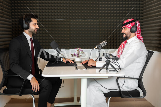 ايماءات الفرح والسرور، رجل عربي خليجي سعودي يرتدي الثوب والشماغ التقليدي مع رجل بالبدلة الرسمية في مقابلة عمل داخل مقر الشركة، معدات وأجهزة تسجيلات الصوت،  اجراء بث صوتي مباشر ( بودكاست ) عبر برامج التواصل الاجتماعي