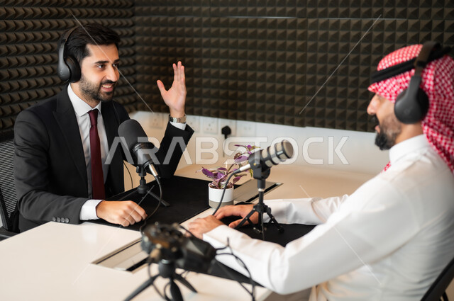 A job interview inside the company headquarters, expressions of happiness and pleasure, a Saudi Gulf Arab man wearing a traditional thobe and shemagh with a man in a formal suit raising his hand up, audio recording equipment and devices, conducting a live audio broadcast (podcast) via social media programs.