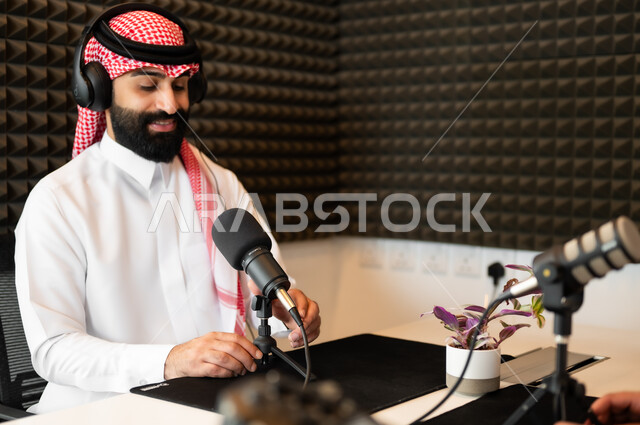 اجراء بث صوتي مباشر ( بودكاست ) عبر برامج التواصل الاجتماعي، رجل عربي خليجي سعودي مبتسم يرتدي الثوب والشماغ التقليدي في مقابلة عمل داخل مقر الشركة، معدات وأجهزة تسجيلات الصوت، ايماءات السعادة والسرور