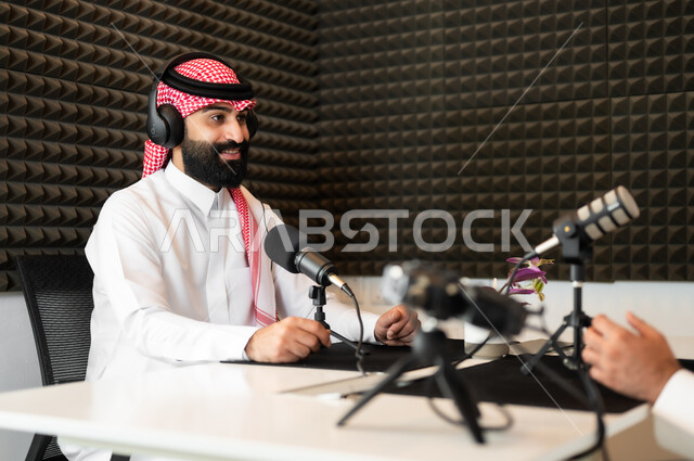 معدات وأجهزة تسجيلات الصوت، استديو تسجيل صوتي ،اجراء بث مباشر ( بودكاست ) عبر برامج التواصل الاجتماعي، رجل عربي خليجي سعودي مبتسم يرتدي الثوب والشماغ التقليدي في مقابلة عمل داخل مقر الشركة،  ايماءات السعادة والسرور