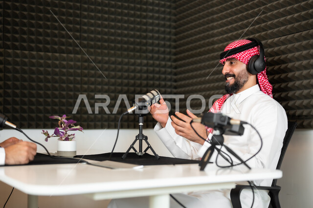 ايماءات الحماس والتفاعل، أجهزة تسجيلات الصوت، اجراء بث مباشر ( بودكاست ) عبر برامج التواصل الاجتماعي، رجل عربي خليجي سعودي مبتسم يرتدي الثوب والشماغ التقليدي في مقابلة عمل داخل مقر الشركة