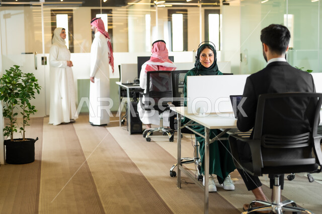 ايماءات الاندماج والسرور،  بيئة العمل المريحة في الشركات السعودية، المشاركة والتعاون في إنجاز الأعمال، رجل عربي خليجي سعودي يرتدي الثوب والشماغ التقليدي مع إمرأة محجبة ترتدي العباءة يقفون داخل مقر الشركة، مهن ووظائف إدارية مكتبية