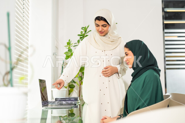 استخدام الأجهزة التقنية الحديثة في المكاتب، اجتماع عمل بين موظفتان عربيتان خليجيتان سعوديتان في غرفة الاجتماعات، مناقشات و حوارات لتحقيق الاستراتيجيات والغايات، التفاهم والتعاون بين الزملاء لتحقيق أهداف الشركة, بيئة العمل المريحة في الشركات السعودية