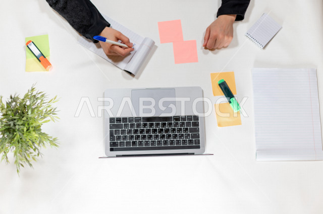  تصوير مقرب من الأعلى , لمساعدة مدير خليجية تكتب المواعيد على ورق ملاحظات أمام اللابتوب على مكتب أبيض , وظيفه ومهن , بيئة عمل , خلفية بيضاء .