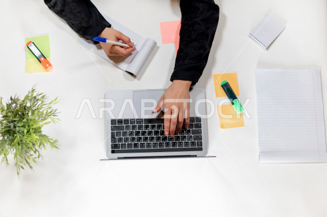 Close-up photography from the top. a Gulf managers assistant , she writes appointments on notes in front of the laptop on a white desk, jobs and professions, work environment, white background.
