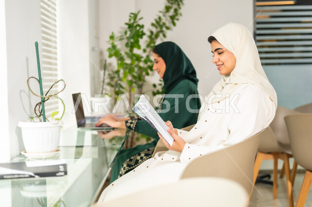 مناقشة المشاريع ومتابعة إستراتيجية العمل، الاستمتاع بقراءة الكتب، إمرأتان عربيان سعوديتان خليجيتان محجبتان ترتديان العباءة، مهن ووظائف نسائية، العمل في الشركات السعودية الراقية, العمل على الحاسوب المحمول داخل المكتب