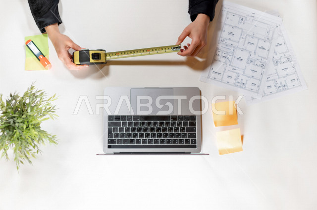  تصوير مقرب من الأعلى , لمهندسة تصميم داخلي عربية سعودية , مهندسة تصمم الأثاث الداخلي أمام اللابتوب على مكتب أبيض , وظيفه ومهن , بيئة عمل , خلفية بيضاء .