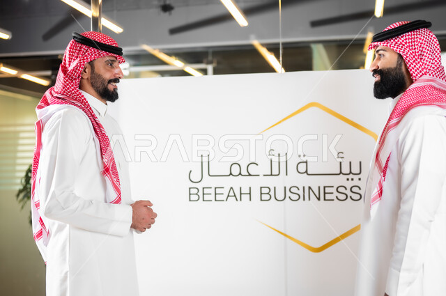 المحادثات و المناقشات عن مفهوم ادارة العمل، الرد على الأسئلة والاستفسارات في المؤتمر التثقيفي،  صورة مقربة لرجلا أعمال عربيان خليجيان سعوديان يرتديان الزي التقليدي والشماغ يقومان بتبادل الأحاديث حول الأعمال المكتبية