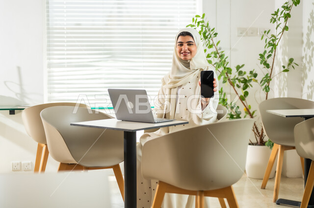 عرض شاشة سوداء فارغة، استخدام الوسائل التقنية الحديثة والمتطورة لإنجاز المهام، مهن ووظائف مكتبية نسائية, إدارة وتنظيم الأعمال ضمن مقر الشركة, امرأة عربية خليجية سعودية محجبة ترتدي العباءة تعمل على الحاسب المحمول, بيئة العمل المريحة في الشركات السعودية