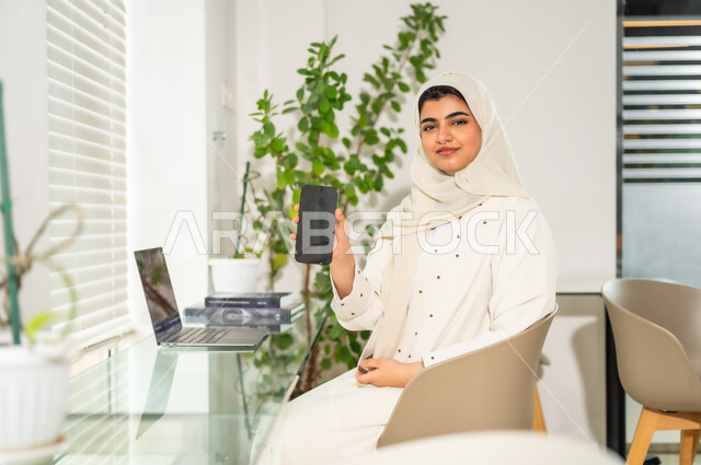 استخدام الوسائل التقنية الحديثة والمتطورة لإنجاز المهام، مهن ووظائف مكتبية نسائية, إدارة وتنظيم الأعمال ضمن مقر الشركة, امرأة عربية خليجية سعودية محجبة ترتدي العباءة تعمل على الحاسب المحمول, بيئة العمل المريحة في الشركات السعودية، عرض شاشة سوداء فارغة