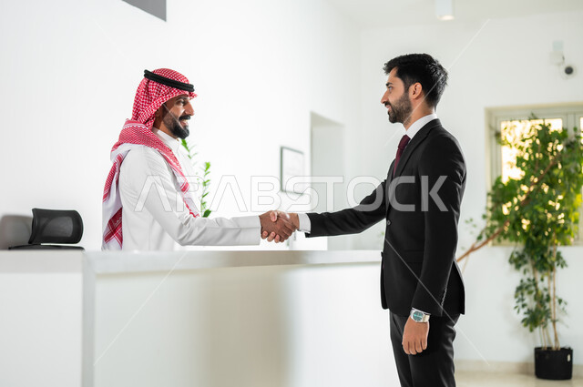 الاتفاق على المشاريع والخطط التجارية, المصافحة والسلام والتحية بتعابير السرور, صورة من الجانب لرجل أعمال عربي خليجي سعودي يرتدي الزي الرسمي يقوم بمصافحة الموظف في الشركة, مهن ووظائف مكتبية