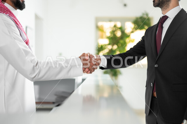 مهن ووظائف مكتبية, الاتفاق على المشاريع والخطط التجارية, المصافحة والسلام والتحية, صورة من الجانب ليد رجل أعمال عربي خليجي سعودي يرتدي الزي الرسمي يقوم بمصافحة الموظف في الشركة