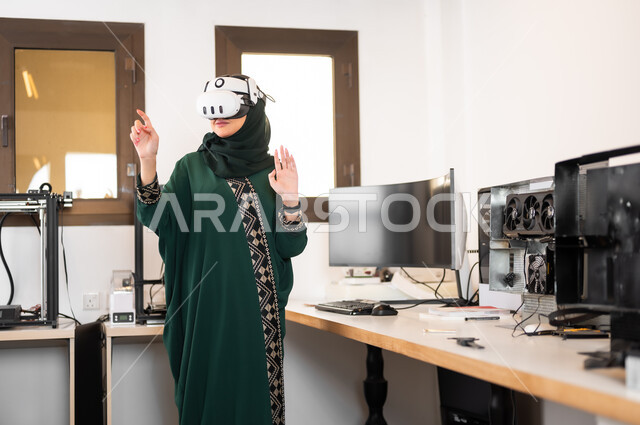الاندماج والتركيز في الواقع الافتراضي، التقدم التقني و التحول الرقمي، استخدام الأجهزة والتفنيات الحديثة المتطورة، محاكاة العالم الخيالي، سيدة عربية خليجية سعودية محجبة ترتدي نظارات ثلاثية الأبعاد تقف بداخل مكتبها وتقوم بالإشارة الى شيء ما