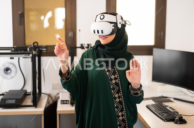 Expressions and gestures of integration and focus in virtual reality, technical progress and digital transformation, the use of advanced modern devices and techniques, simulating the imaginary world, a veiled Saudi Gulf Arab woman wearing 3D glasses standing inside her office and pointing at something