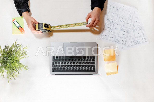  تصوير مقرب من الأعلى , لمهندسة تصميم داخلي عربية سعودية , مهندسة تصمم الأثاث الداخلي أمام اللابتوب على مكتب أبيض , وظيفه ومهن , بيئة عمل , خلفية بيضاء .