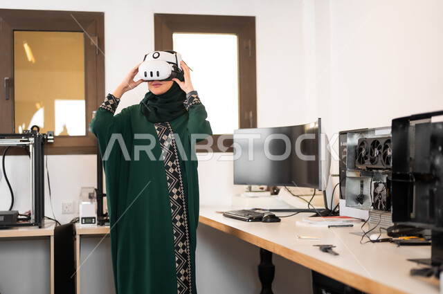 Digital transformation and technical progress, the use of advanced modern devices and techniques, simulating the imaginary world, a veiled Saudi Gulf Arab woman wearing 3D glasses standing inside her office, expressions and gestures of integration and concentration in virtual reality