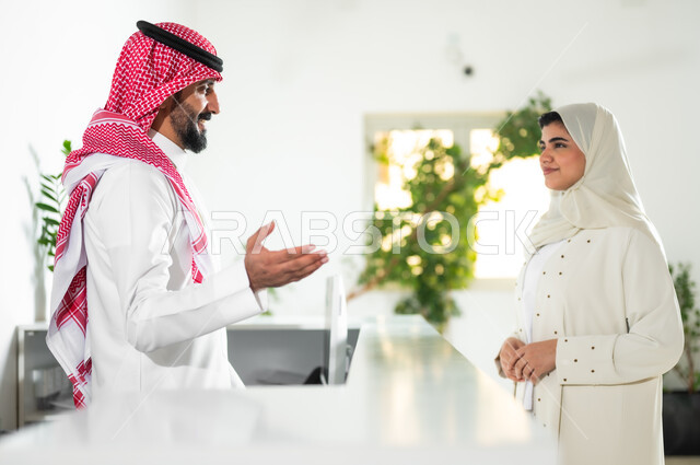 البشاشة وحسن الاستقبال, الحوار والنقاش وتقديم الخدمات للعملاء, صورة مقربة من الجانب لشابة عربية خليجية سعودية ترتدي العباءة والحجاب تقوم بالاستفسار في مكتب الخدمة, مهن ووظائف سعودية, بيئة العمل المريحة في الشركات الراقية