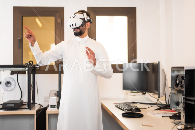 لعب ألعاب الفيديو ثلاثية الأبعاد، الأجهزة والتقنيات الحديثة والمتطورة، مشاهدة أفلام عبر نظارات الواقع الإفتراضي، التفاعل ومحاكاة مع العالم الخيالي، رجل عربي خليجي سعودي يرتدي الزي التقليدي يقوم بالنقر والإشارة الى شيء ما