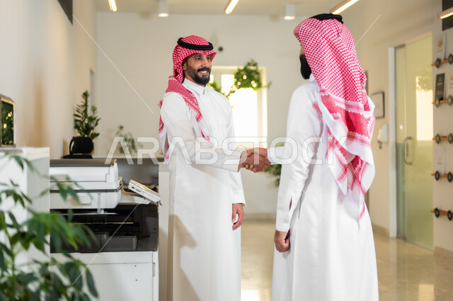 العمل في الشركات الخليجية الراقية, التحية والسلام والاتفاق على صفقات عمل ناجحة, رجلا أعمال عربيان خليجيان سعوديان يرتديان الثوب التقليدي والشماغ يقومان بالمصافحة بتعابير السرور, مهن ووظائف سعودية