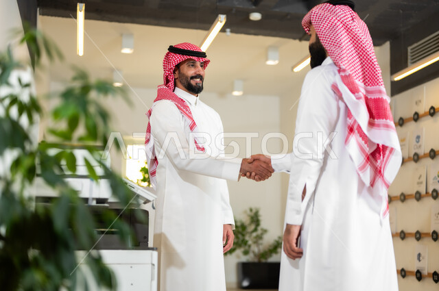 العمل في الشركات الخليجية الراقية, التحية والسلام والاتفاق على صفقات عمل ناجحة, رجلا أعمال عربيان خليجيان سعوديان يرتديان الثوب التقليدي والشماغ يقومان بالمصافحة بتعابير السرور, مهن ووظائف سعودية