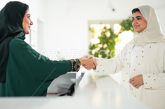 عقد اتفاقيات عمل ناجحة بتعابير التحية والسلام , صورة مقربة من الجانب لشابة عربية خليجية سعودية ترتدي العباءة والحجاب تقوم بمصافحة موظفة الاستقبال, العمل في الشركات السعودية الراقية