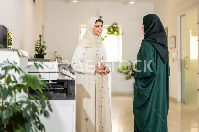حوارات ونقاشات حول مفهوم ادارة العمل، سيدتا أعمال عربيتان خليجيتان سعوديتان محجبتان ترتديان عباءات عصرية تقومان بتبادل الأحاديث والحوارات, مهن ووظائف نسائية مكتبية, بيئة العمل الراقية في الشركات الخليجية
